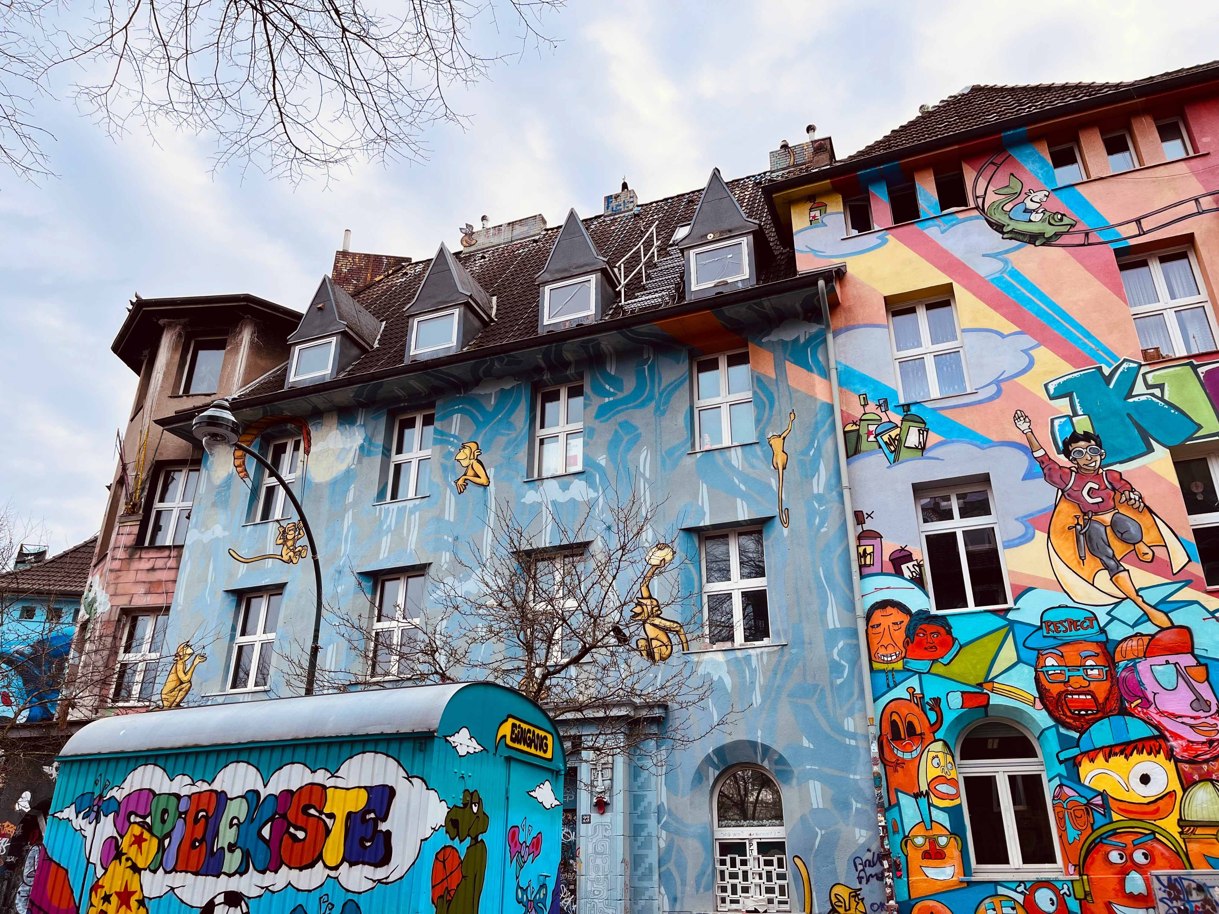 Tourismus NRW e.V., Bauwagen "Spielekiste" vor bunten Fassaden der Kiefernstraße, Düsseldorf