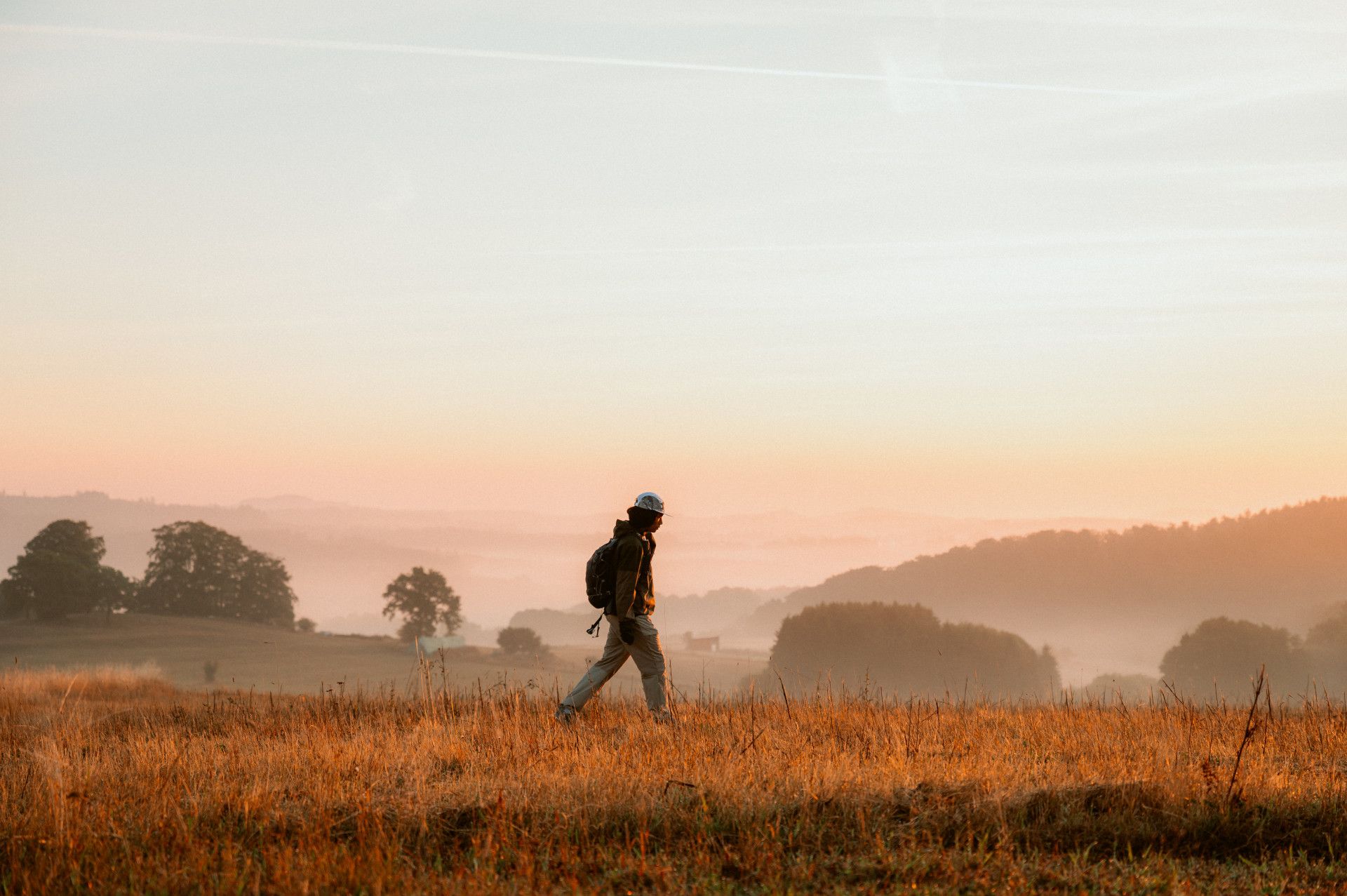 Wanderer bei Sonnenaufgang, im Hintergrund Nebel, Bäume und Felder