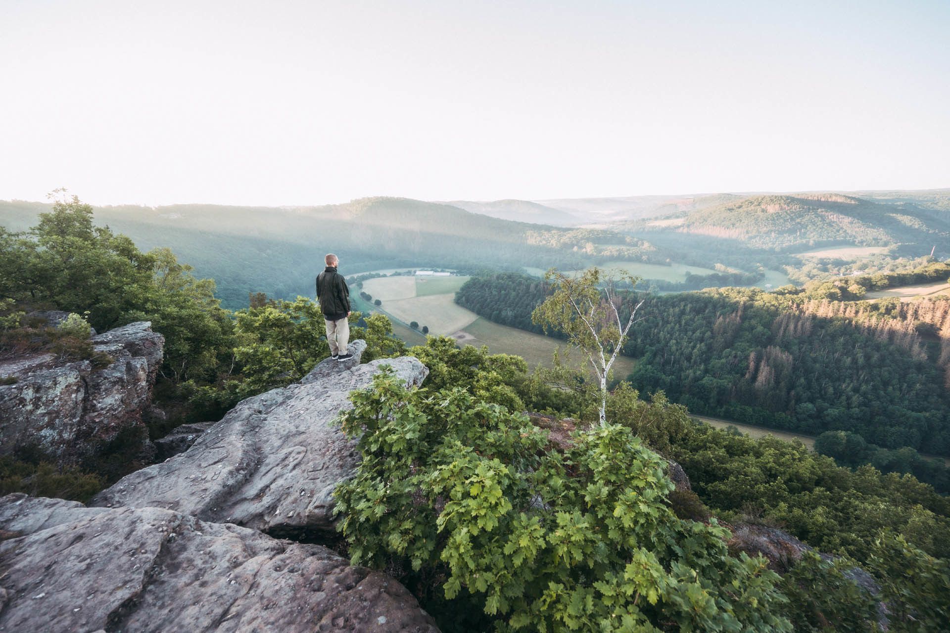 Wanderer steht auf Felsen und blickt über die Landschaft zu seinen Füßen.