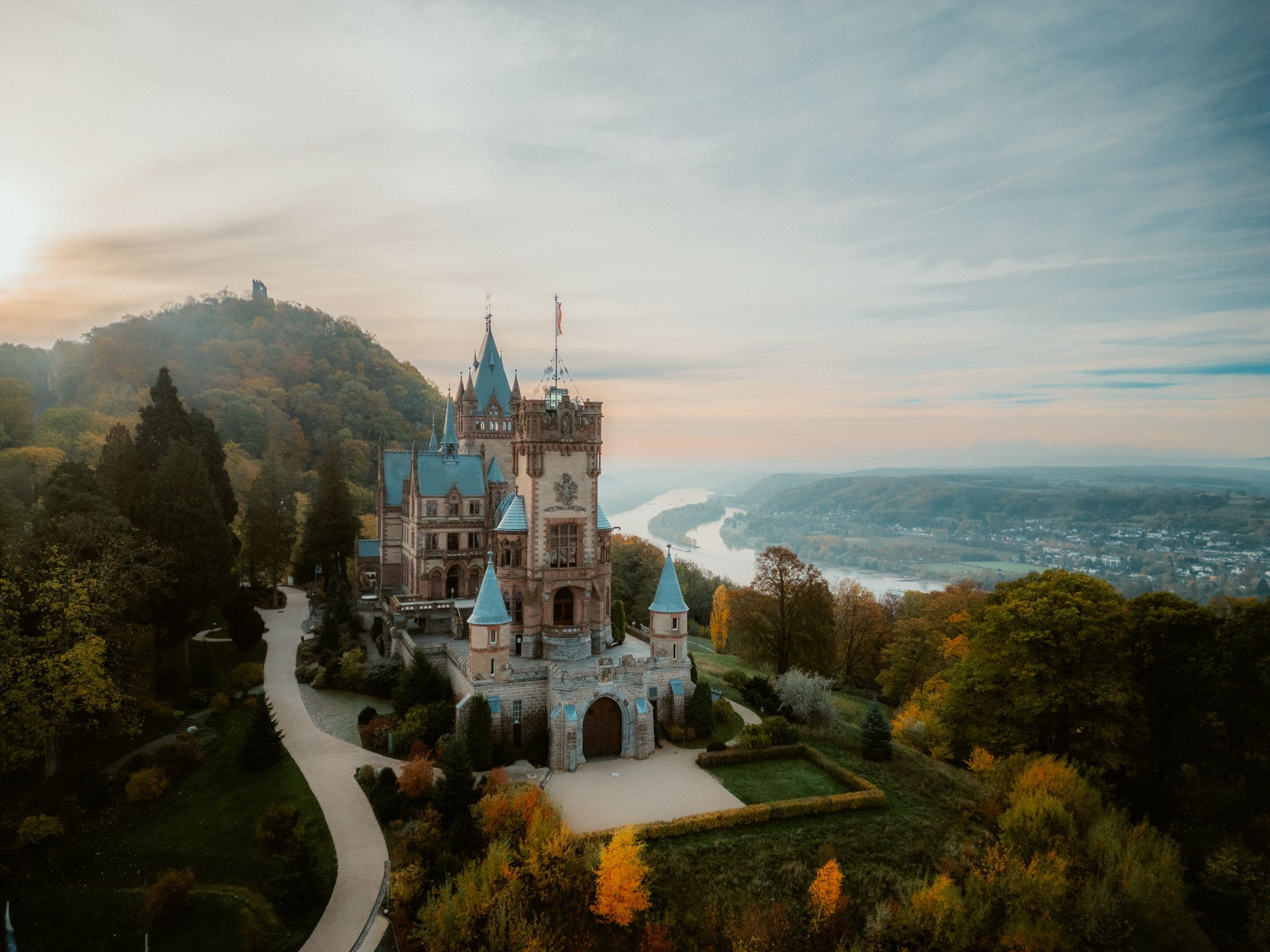 Schloss mit Türmen auf Berg in hügeliger Landschaft mit Fluß im Hintergrund