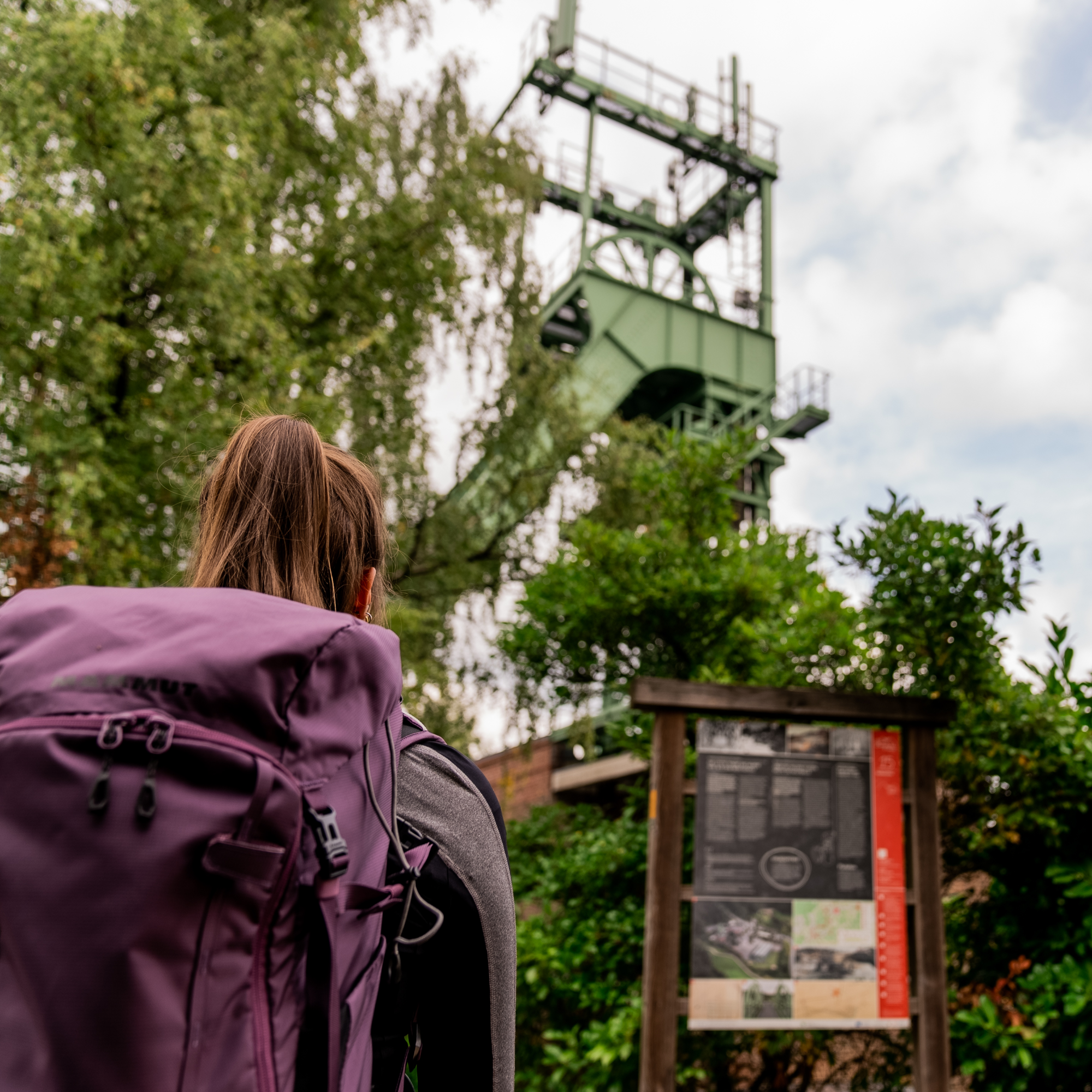 Hiker stands in front of a headframe with an information board in front of it